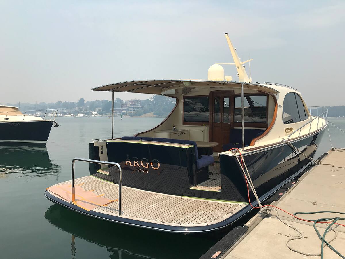 Freshly detailed timber-decked launch with a navy hull moored at a marina