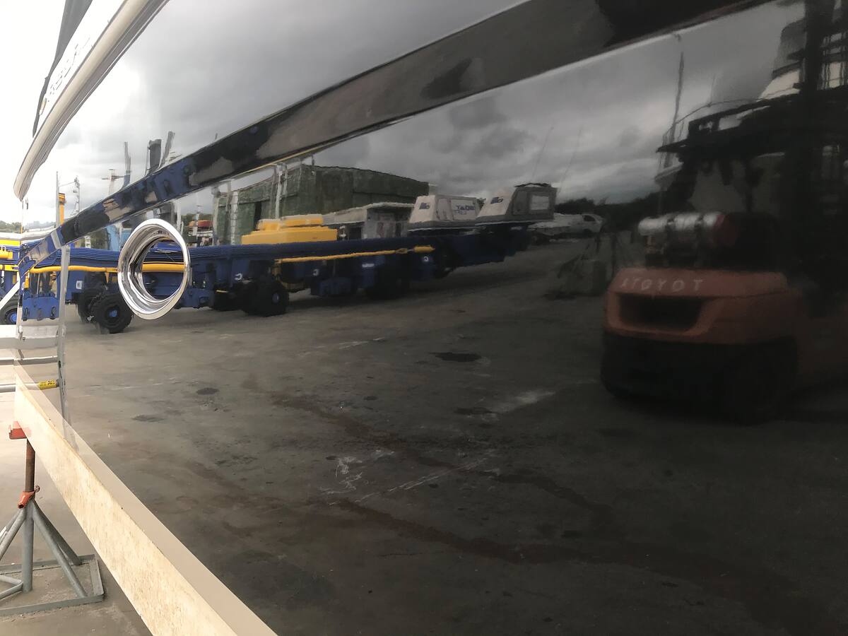 Polished black hull reflecting the boatyard like a mirror